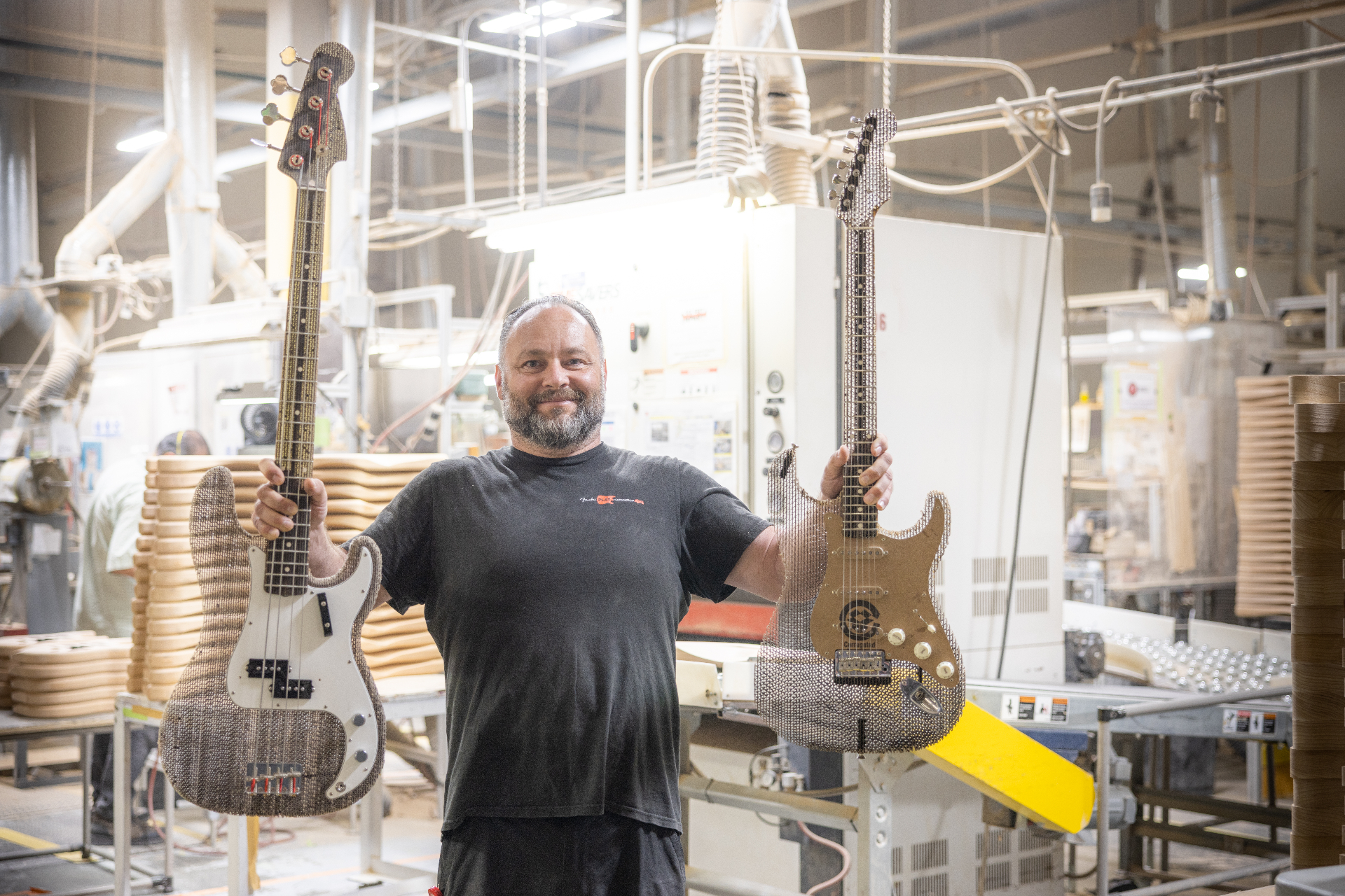 Builder holding the finished cardboard Precision Bass and Stratocaster side by side