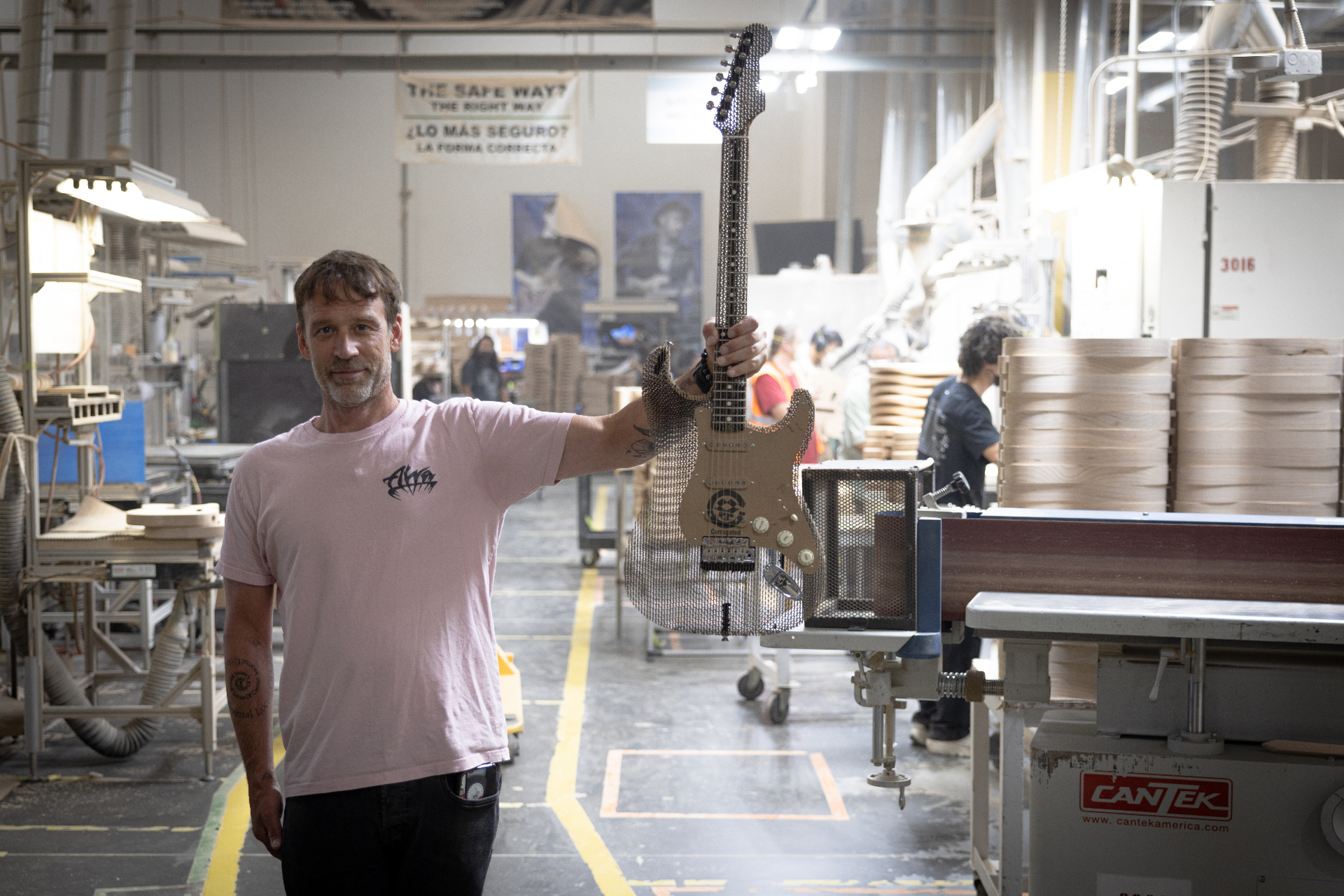 Builder holding the finished cardboard Stratocaster on the factory floor